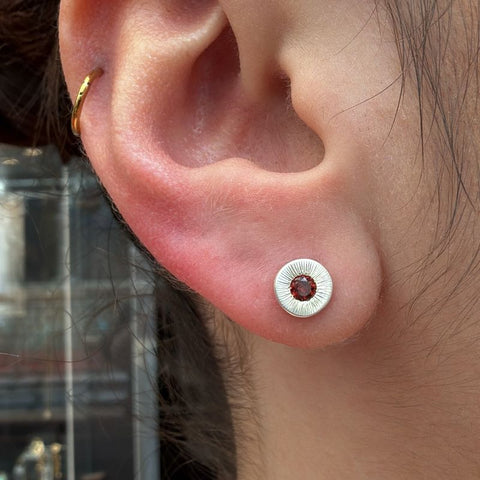 Close-up of an ear with a silver earring featuring a red gemstone.
