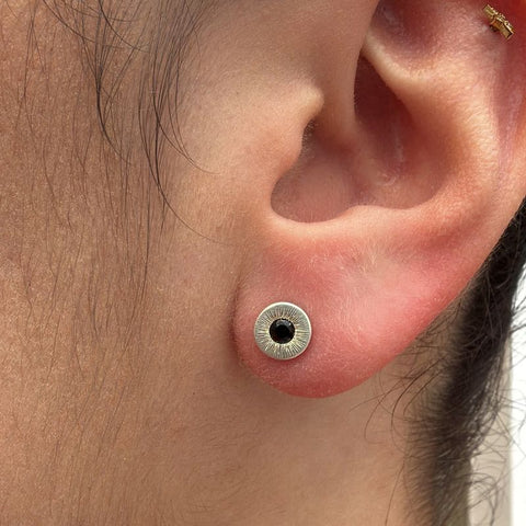 Close-up of an ear with a silver and black spinel stud earring.