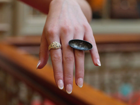 Hand wearing two rings, one silver and one blackened silver with a blurred background