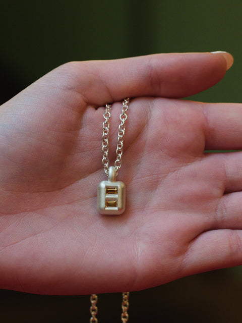 Silver chain with a square pendant that has 2 stones held in a hand against a blurred background
