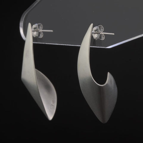 Silver earrings on a clear stand against a black background