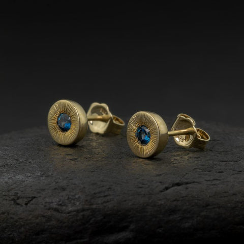 Gold earrings with blue sapphires on a dark surface