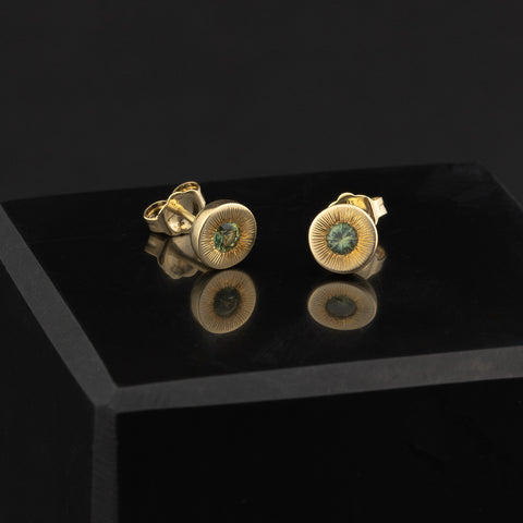 Gold stud earrings with green sapphire gemstones on a black surface