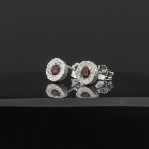 Silver earrings with red gemstones on a black reflective surface
